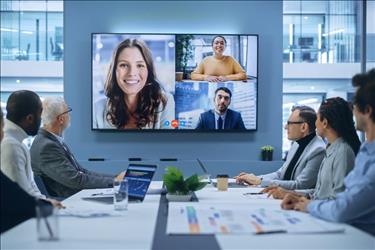 meeting in a conference room with several remote employees on screen