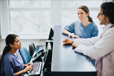 medical receptionist behind her desk looking up at two medical team members having a conversation