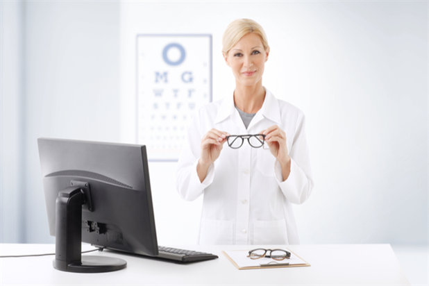Happy hospital optometrist posing for camera with pair of eyeglasses