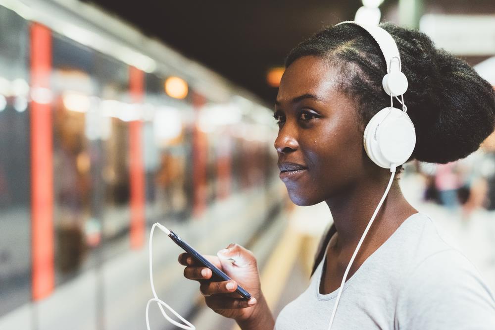 Smiling woman listening to something on her phone while she waits for the train