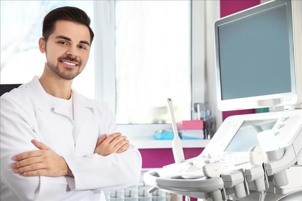 smiling diagnostic medical sonographer standing in front of his equipment in the exam room