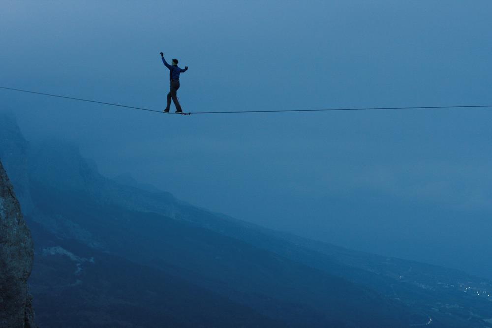 tightrope walker spanning a mountain pass at twilight