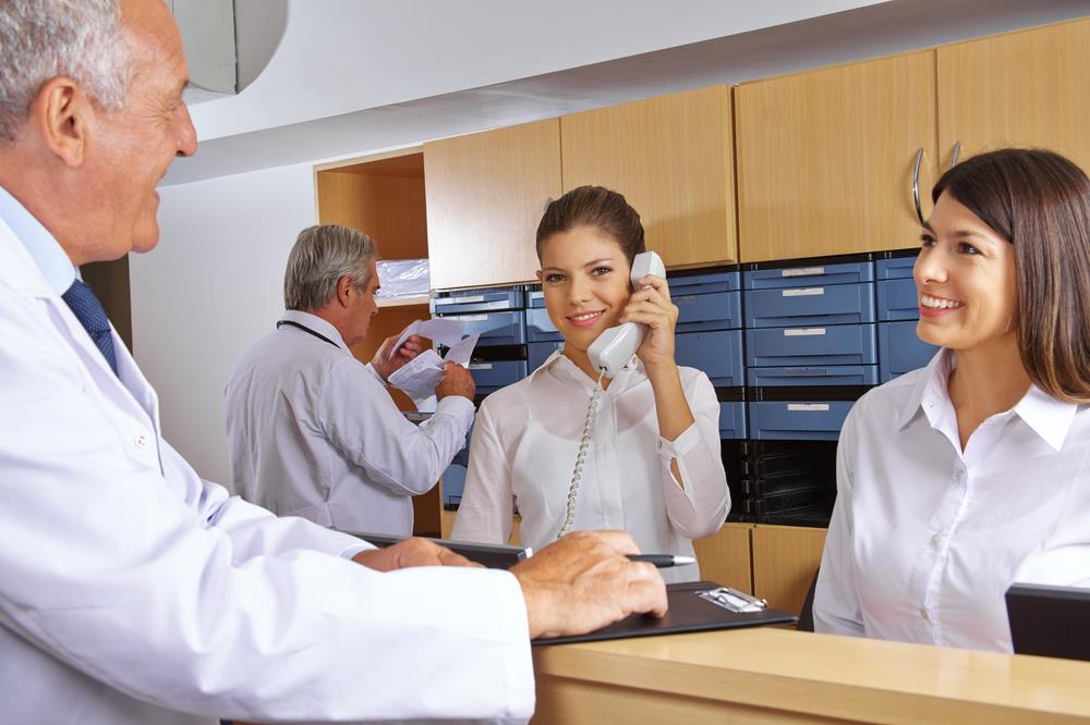healthcare administrators behind the reception desk speaking on the phone and to a physician