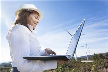 female environmental engineer in the field on her laptop with wind turbines in the background