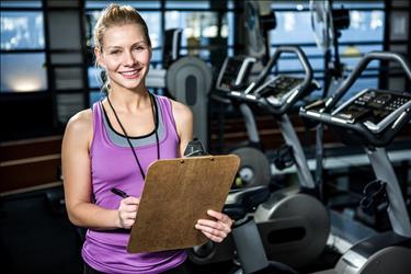 smiling fitness instructor holding a clipboard in a gym