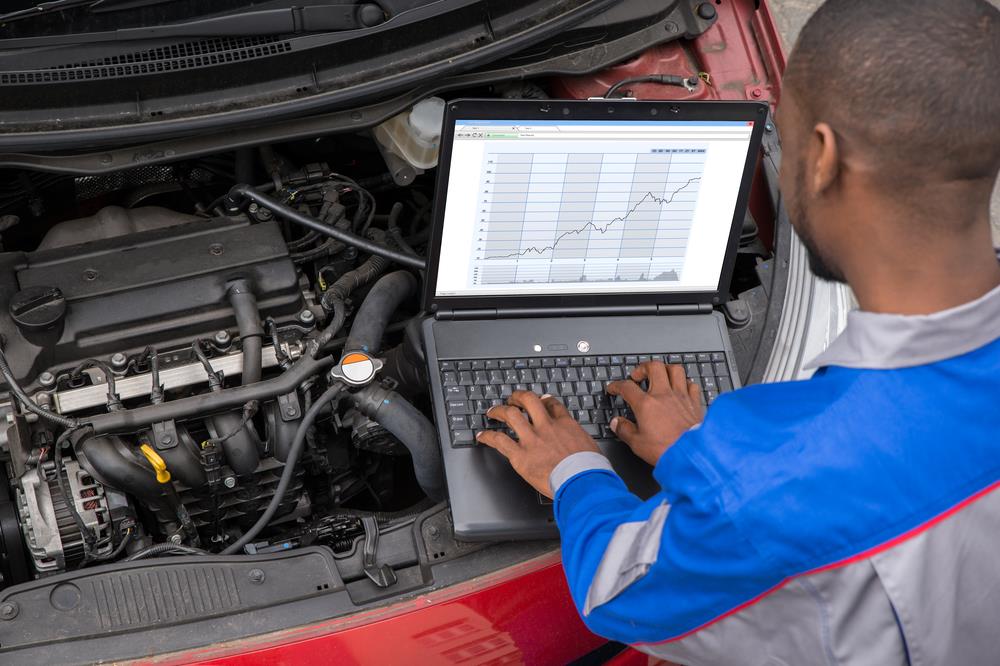 automotive technician using a laptop while diagnosing a car