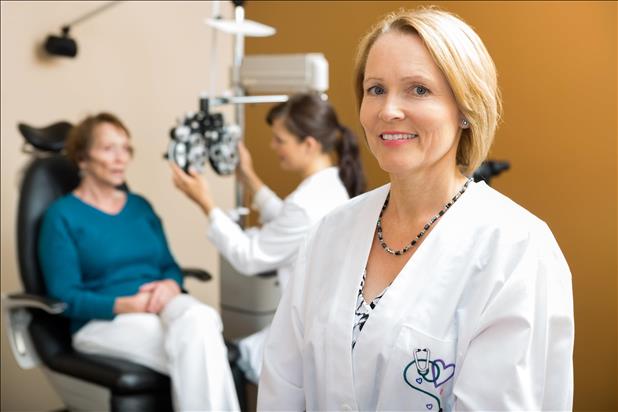 Portrait of confident eye doctor with colleague examining patient in background