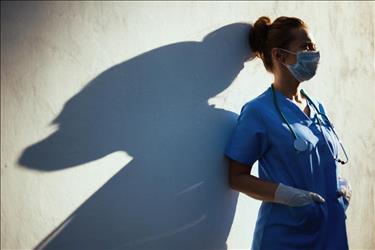 tired medical professional wearing a mask while leaning on a wall outside